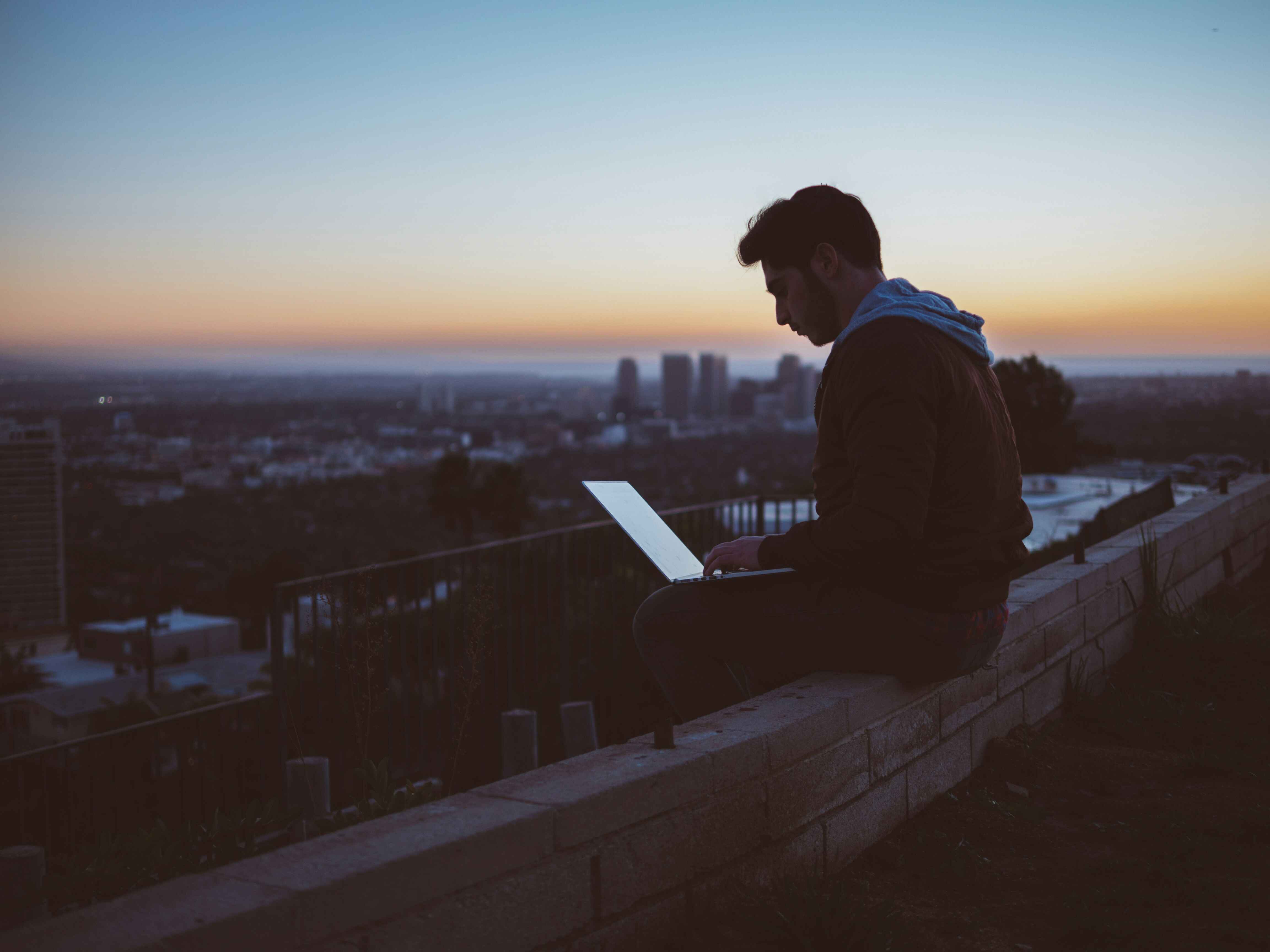 boy on laptop sat on a rooftop with the skyline in the background